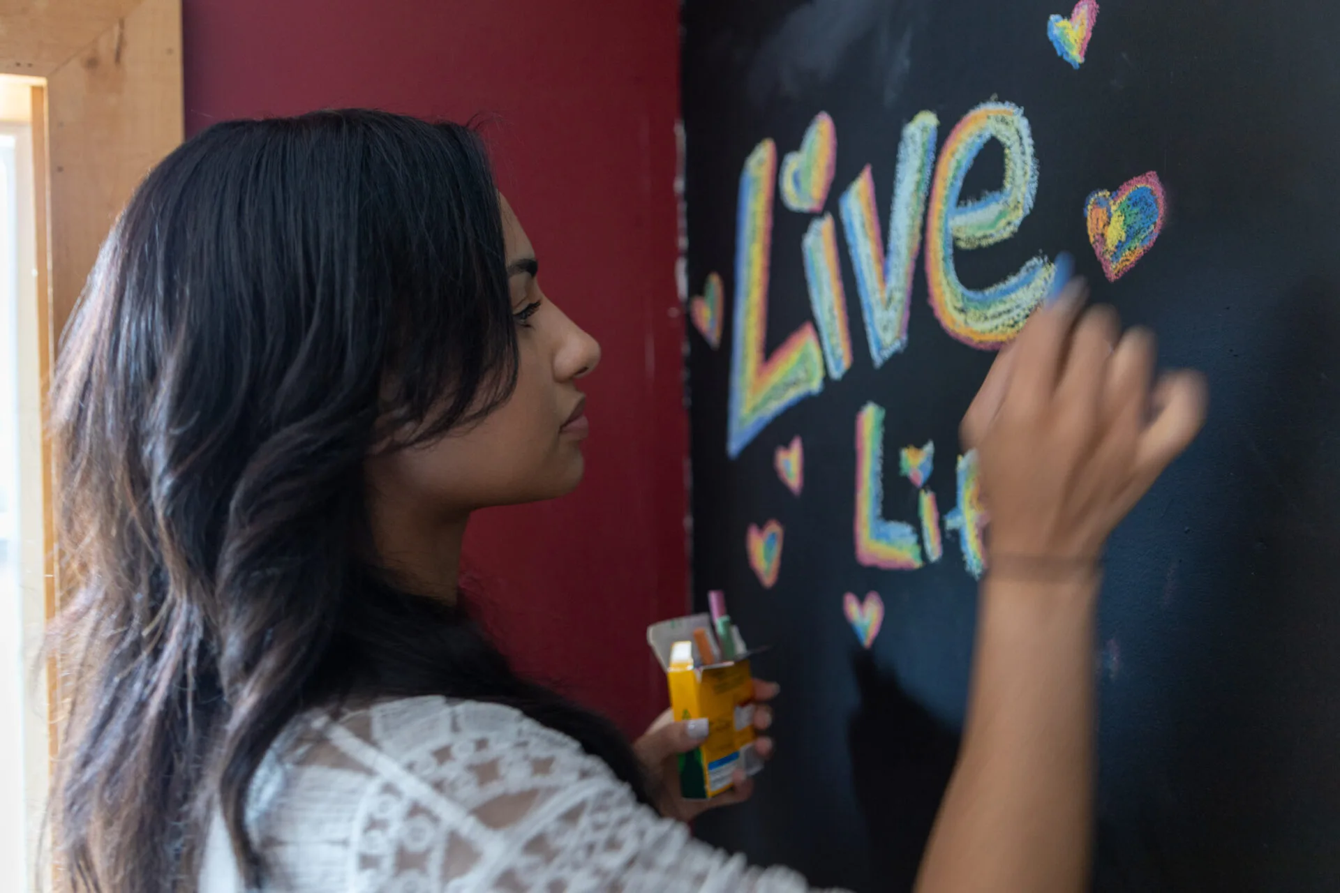 A Woman drawing the word Live in rainbow chalk at Pachamama Sanctuary